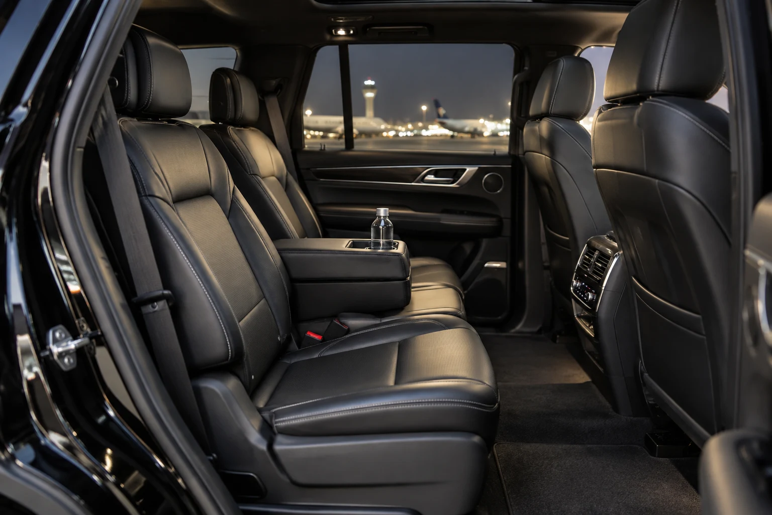 Illustrative premium SUV cabin with black leather passenger seats and airport lights outside.
